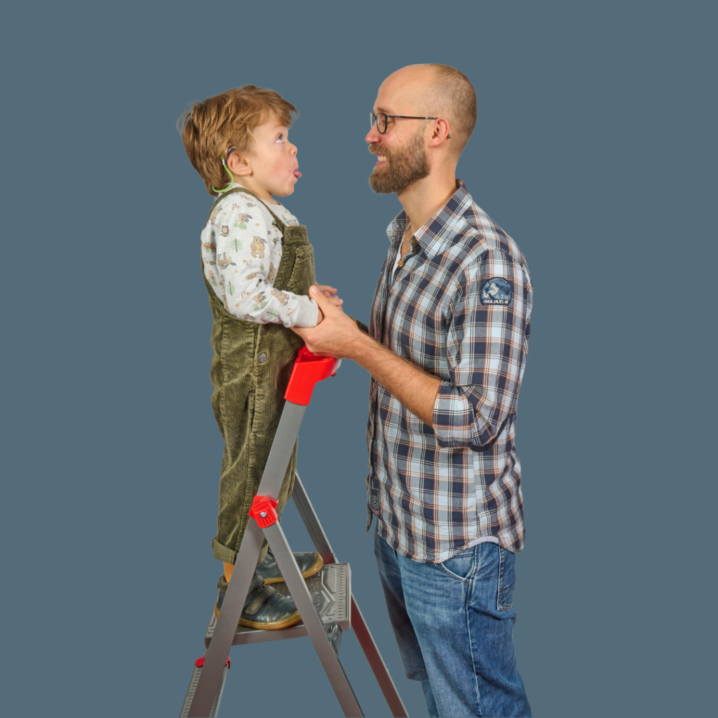 Ein Mann sieht einen Jungen an, der auf einer Leiter steht und die Zunge herausstreckt